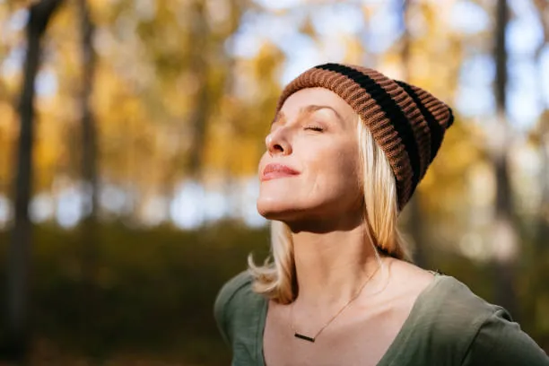 A woman outdoors in autumn light with her eyes closed